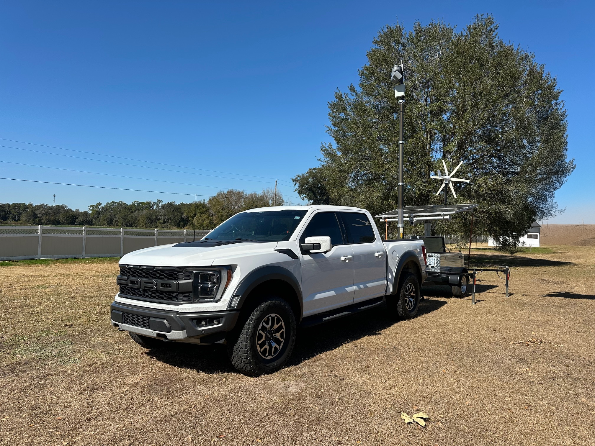 Helios Tactical Sentinel field deployment with truck, trailer, mast, solar panels and wind turbine